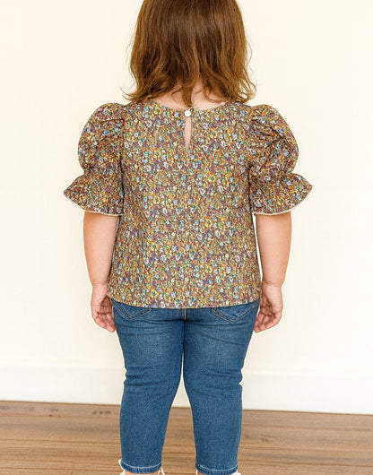 Back view of Puff Sleeve Blouse child wearing a floral blouse and blue jeans against a plain background