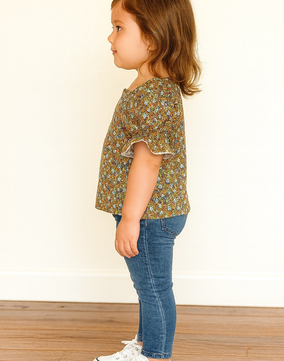 Side view of child wearing a floral Puff Sleeve Blouse and blue jeans on a plain background