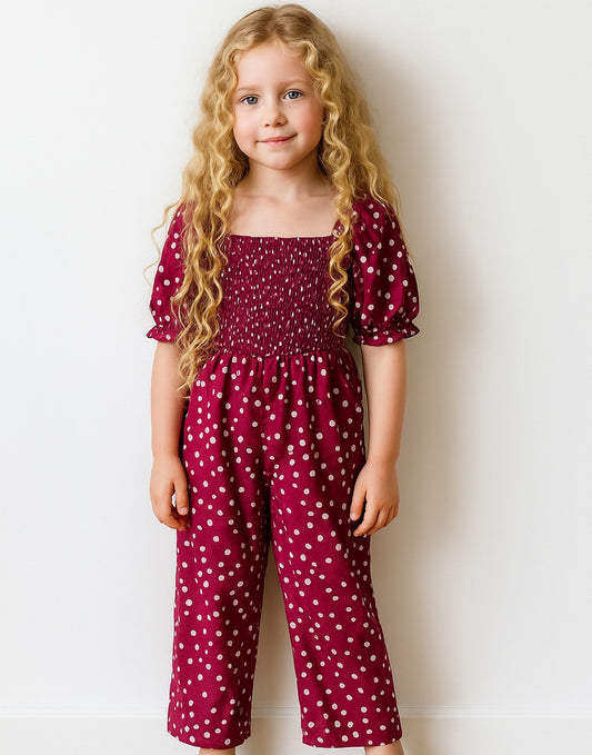 Young girl wearing a maroon Puff Sleeve Shirred Jumpsuit with white polka dots against a plain background