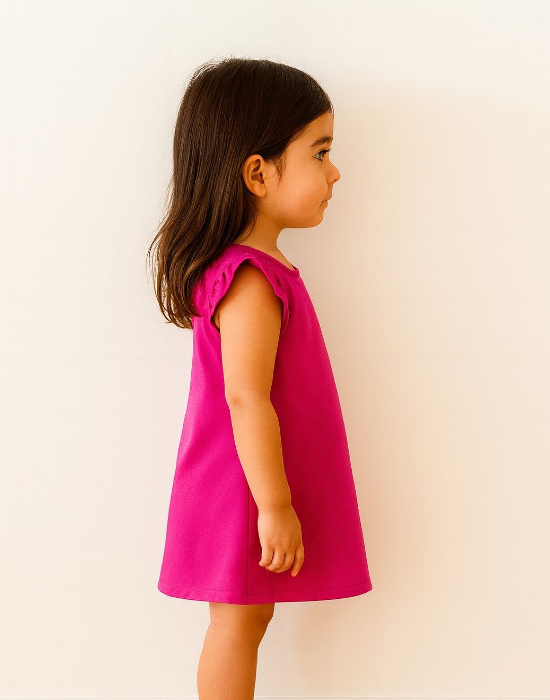 Side view of young girl wearing a pink Ruffle Sleeve A-Line Dress against a plain background