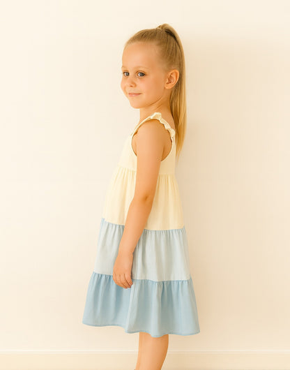 Side view of young girl wearing a Ruffle Sleeve Cami Dress with a yellow top and blue striped skirt on a beige background