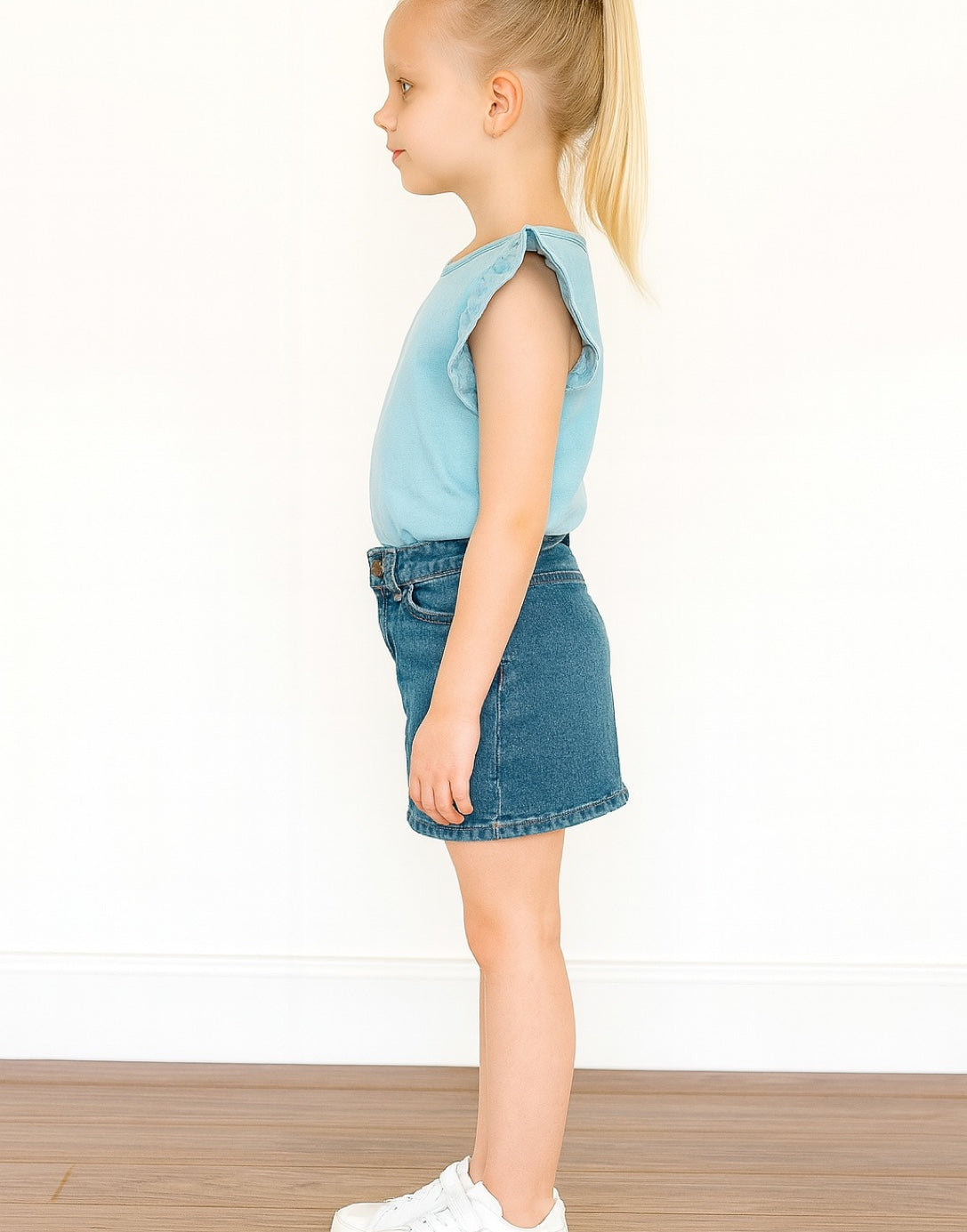 Side view of young girl wearing a Ruffle Tee and denim skirt on a white background
