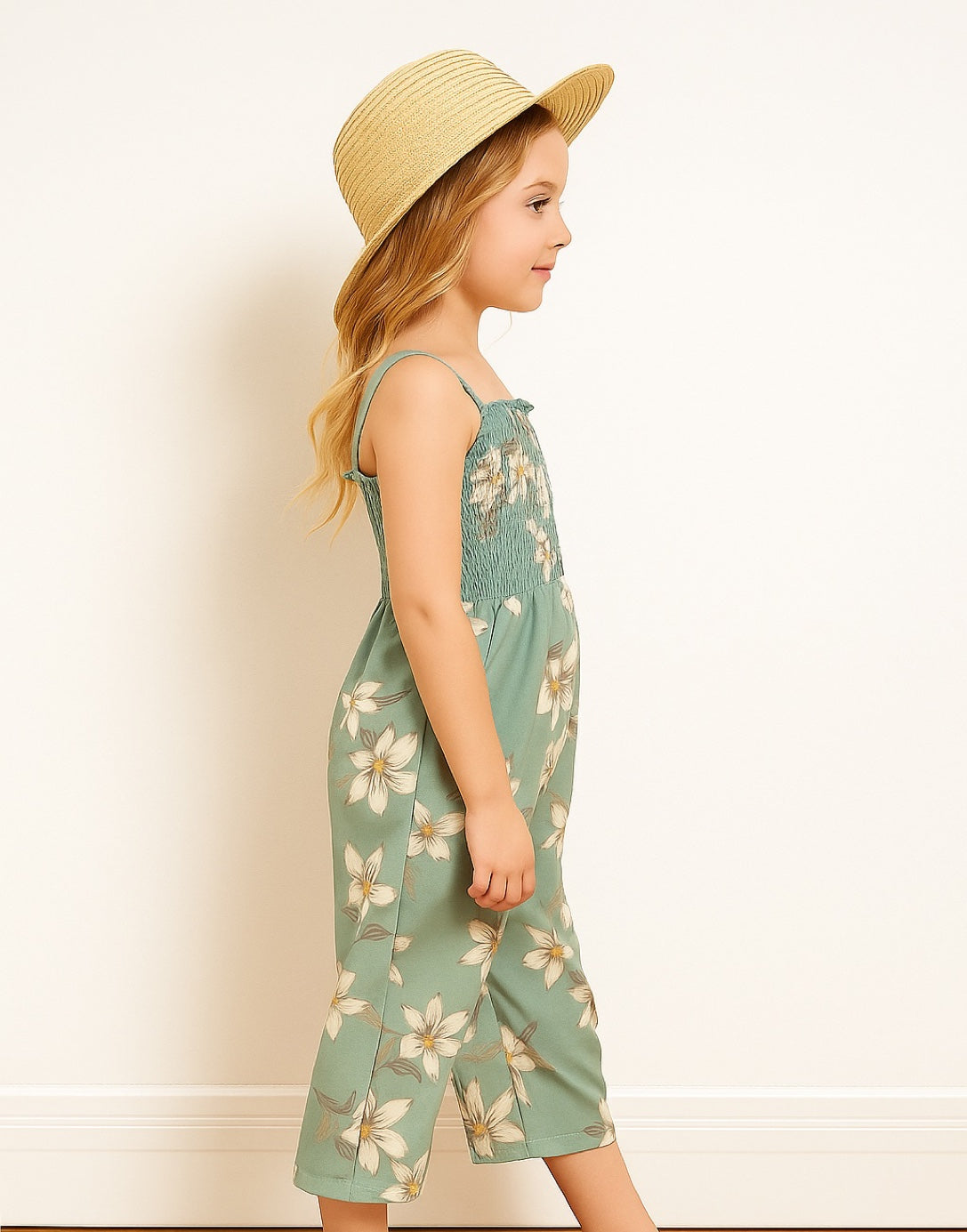 Side view of young girl wearing a floral Shirred Cami Jumpsuit standing indoors with a neutral background.