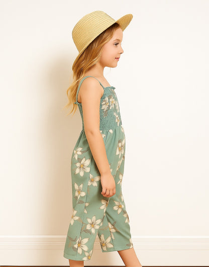Side view of young girl wearing a floral Shirred Cami Jumpsuit standing indoors with a neutral background.