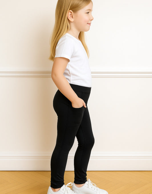 Side view of young girl wearing a white t-shirt and Side Pocket Leggings against a plain wall.