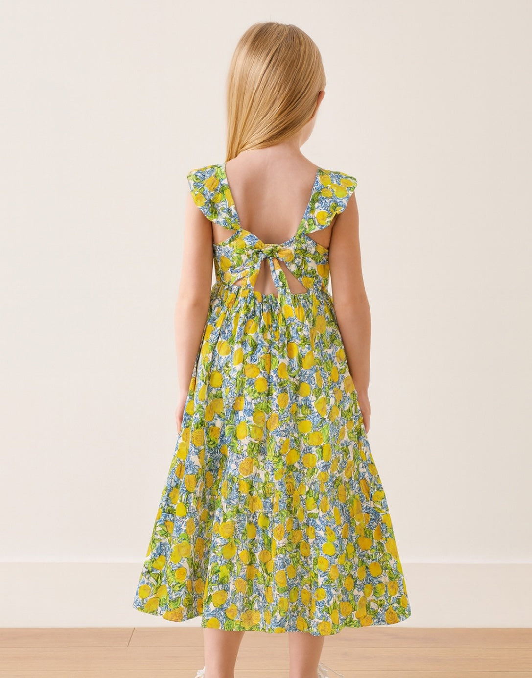 Back view of girl wear a blue and yellow floral print Tie Back Ruffled Sleeve Maxi Dress with a plain background.