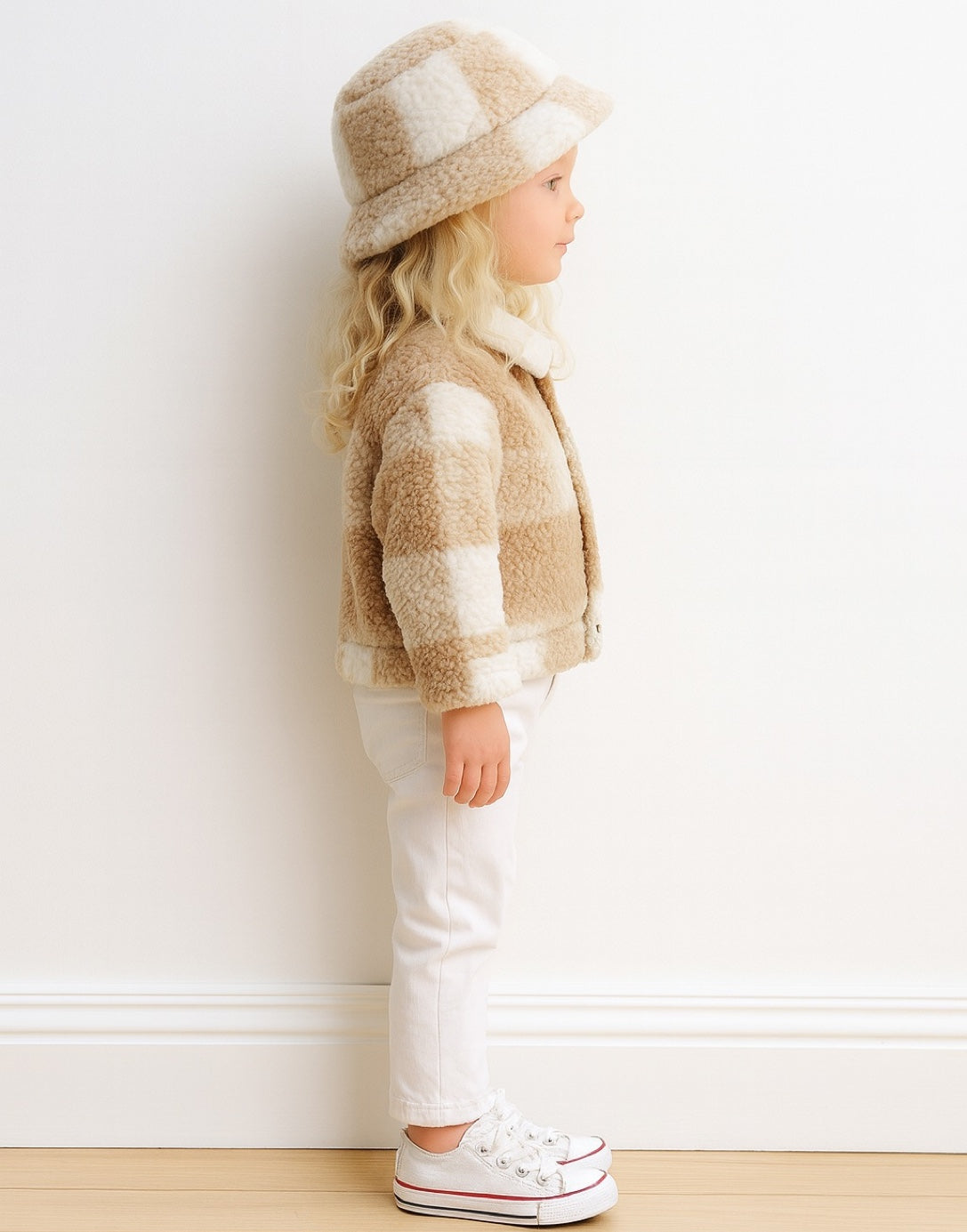 Side view of child wearing a beige and white striped Teddy Jacket with a matching hat against a white wall.