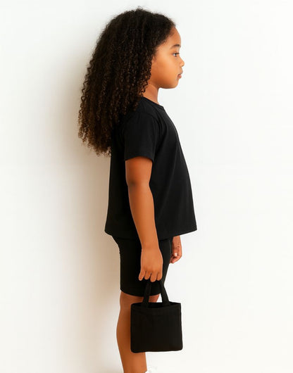 Side view of child wearing a black Tee and Biker Shorts holding a small black handbag against a white background.