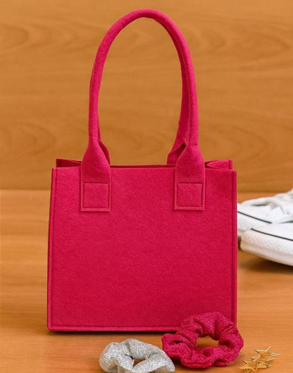 Back view of pink girls tote bag with hair scrunchies and decorative stars on a wooden surface.