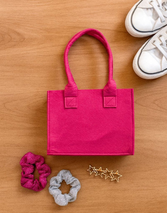 Pink girls tote bag with hair scrunchies and decorative stars on a wooden surface.