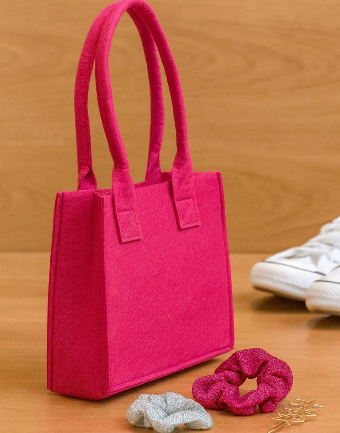 Side view of pink girls tote bag with hair scrunchies and decorative stars on a wooden surface.