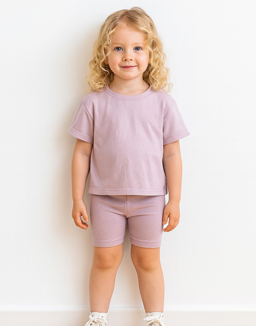 Young child wearing a light purple t-shirt and shorts set on a white background
