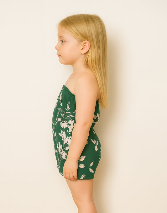 Side view of young girl wearing a green floral strapless Tube Romper against a plain background.