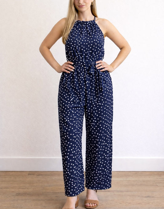 Woman wearing a navy blue Halter Belted Jumpsuit with white polka dots against a plain background.