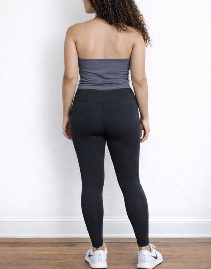 Back view of woman wearing a gray Halter Tank Top and black leggings against a white wall.