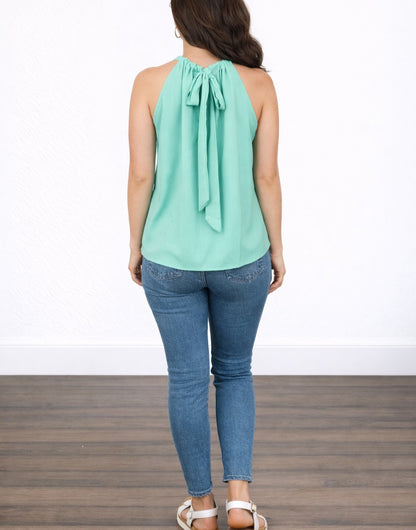 Back view of woman wearing a light green Sleeveless Tie Back Halter Top and blue jeans on a white background