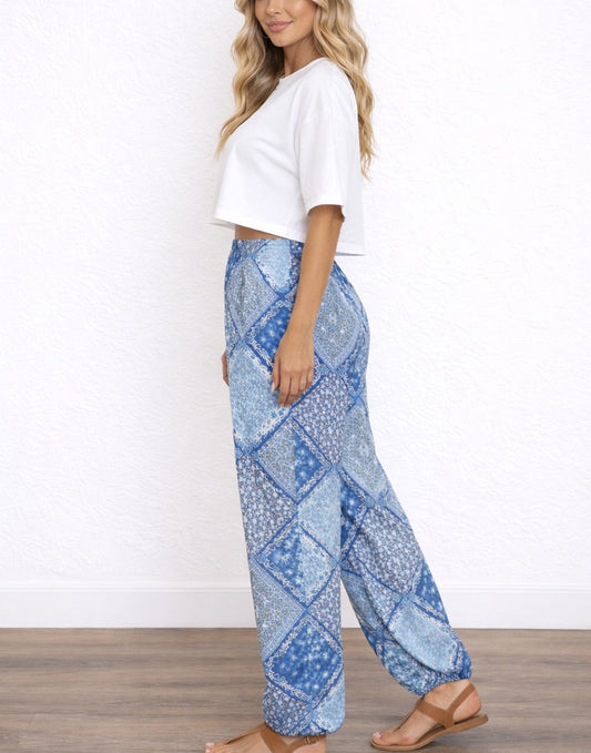 Side view of woman wearing blue patterned Harem Pants and a white top on a white background.