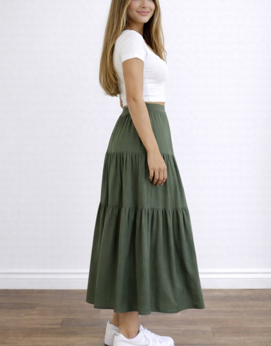 Side view of woman wearing a white top and green High Waist Tiered Hem Maxi Skirt on a plain background.