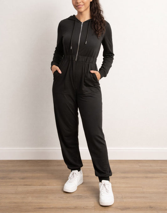 Woman wearing a black Zip Up Hooded Jumpsuit with white sneakers on a wooden floor.