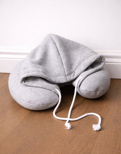 Side view of gray Hoodie Travel Pillow on a wooden floor with a white wall background.