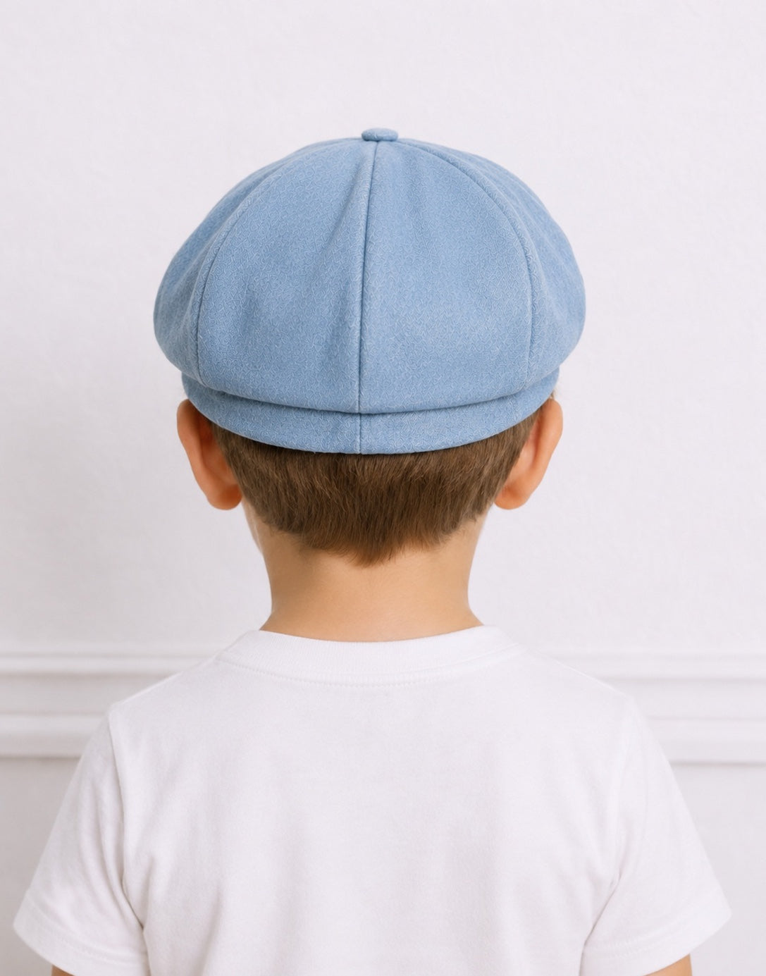 Back view of a young boy wearing a light blue denim Baker Boy Cap with a white crew neck tee shirt.