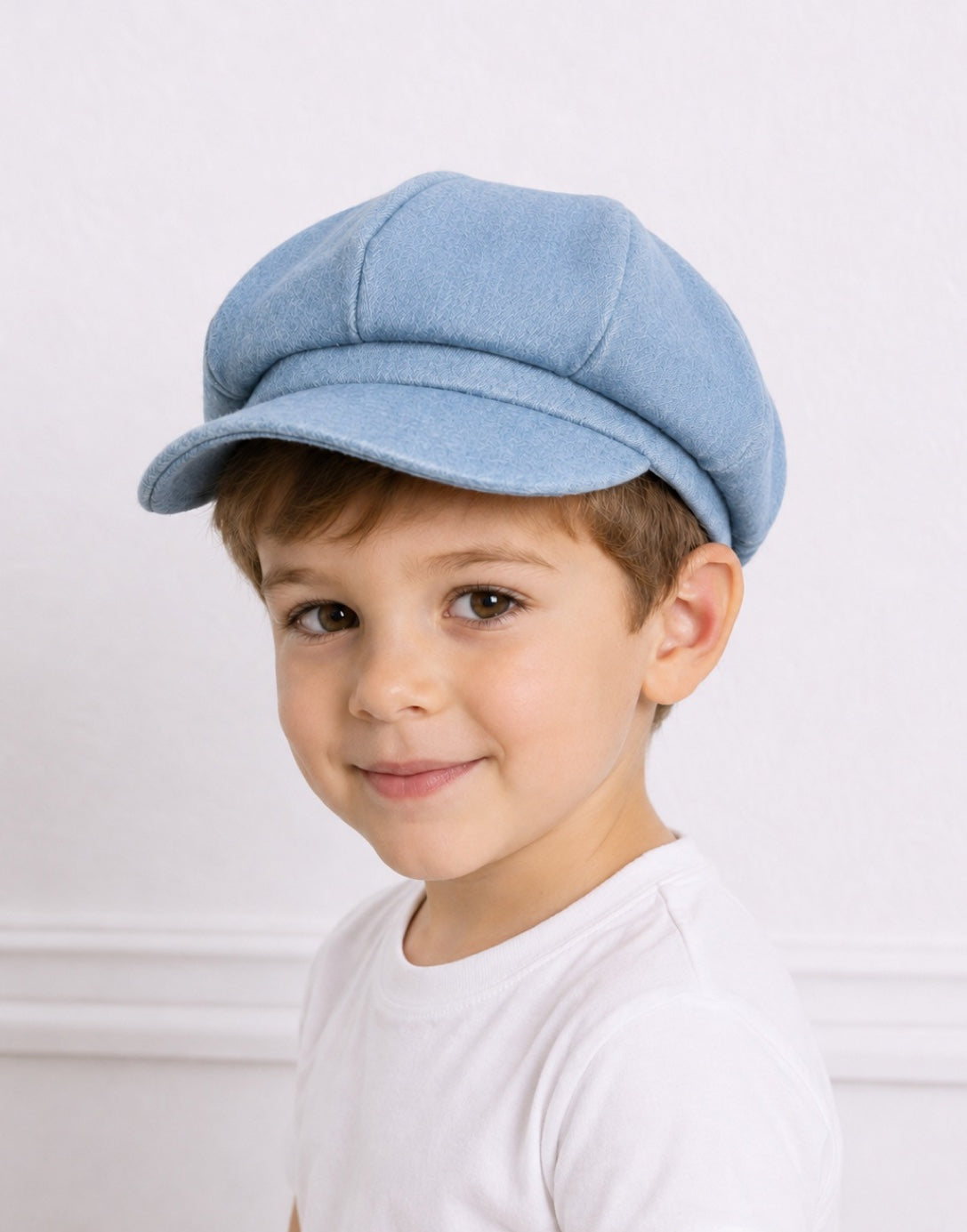 Side view of a young boy wearing a light blue denim Baker Boy Cap with a white crew neck t-shirt.