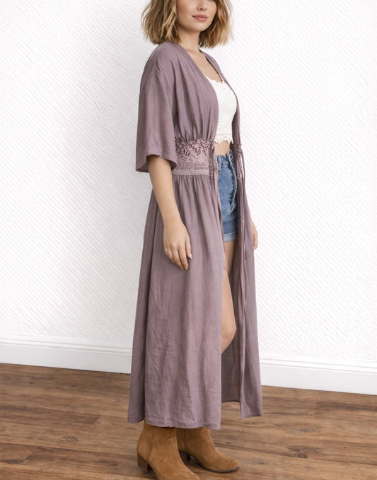Side view of woman wearing a long mauve Lace Trim Kimono Sleeve Long Jacket over a white lace top and denim shorts, standing on a wooden floor.