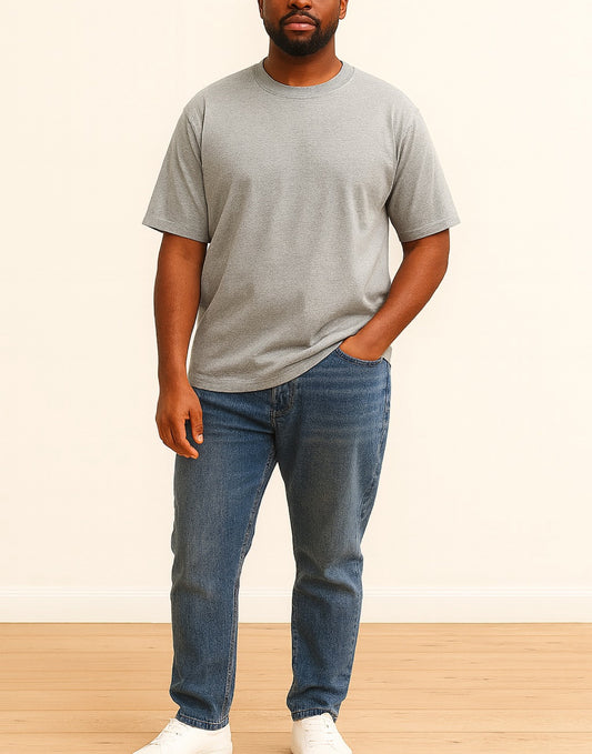 Man wearing a gray Oversized T-Shirt and blue jeans standing against a plain background