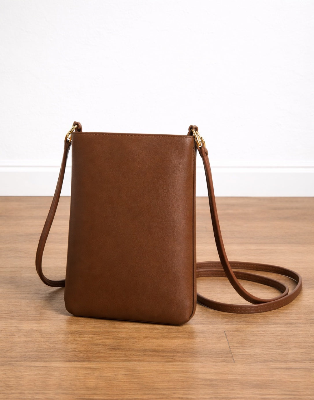 Side view of brown leather Mini Crossbody Bag on a wooden surface with a white background.