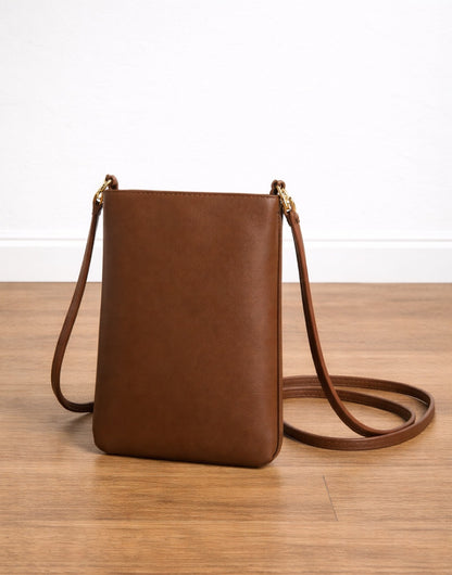 Side view of brown leather Mini Crossbody Bag on a wooden surface with a white background.