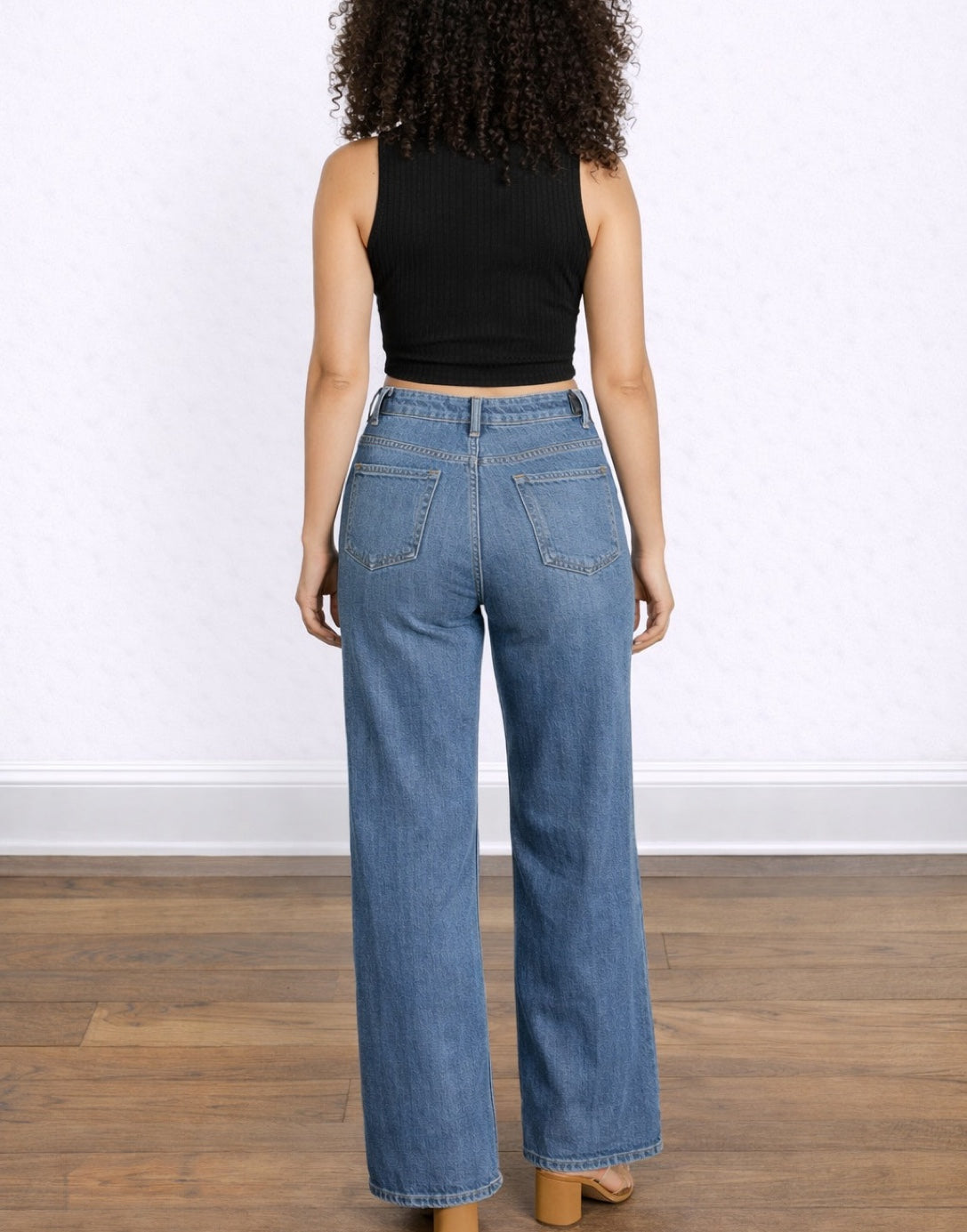 Back view of woman wearing blue jeans and a black Mock Neck Crop Tank Top on a white background.