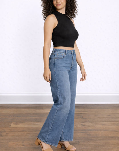 Side view of woman wearing blue jeans and a black Mock Neck Crop Tank Top on a white background.