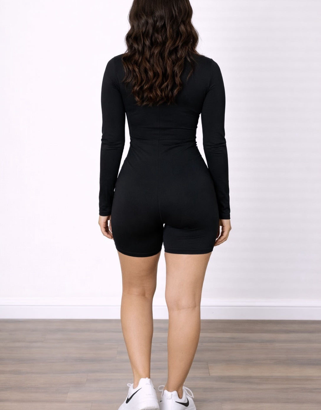 Back view of woman wearing a black long-sleeve Mock Neck Unitard Romper with a white background.