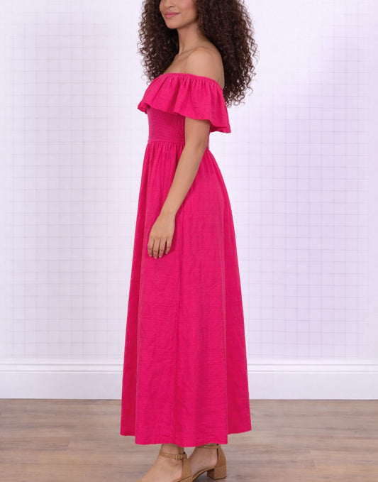 Side view of woman wearing a bright pink Off Shoulder Maxi Dress against a white background. 