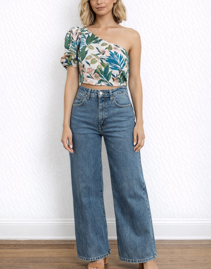 Woman wearing a floral One Shoulder Puff Sleeve Crop Top and blue jeans against a white wall.