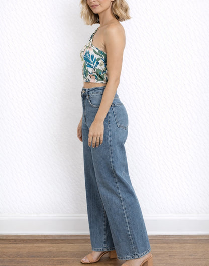 Side view of woman wearing a floral One Shoulder Puff Sleeve Crop Top and blue jeans against a white wall.