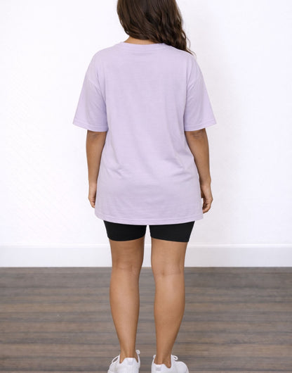 Back view of woman wearing a light purple Oversized T-Shirt and black shorts on a white background.
