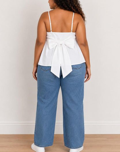Back view of woman wearing a white Plus Size Bow Back Babydoll Cami Top and blue jeans against a plain background.