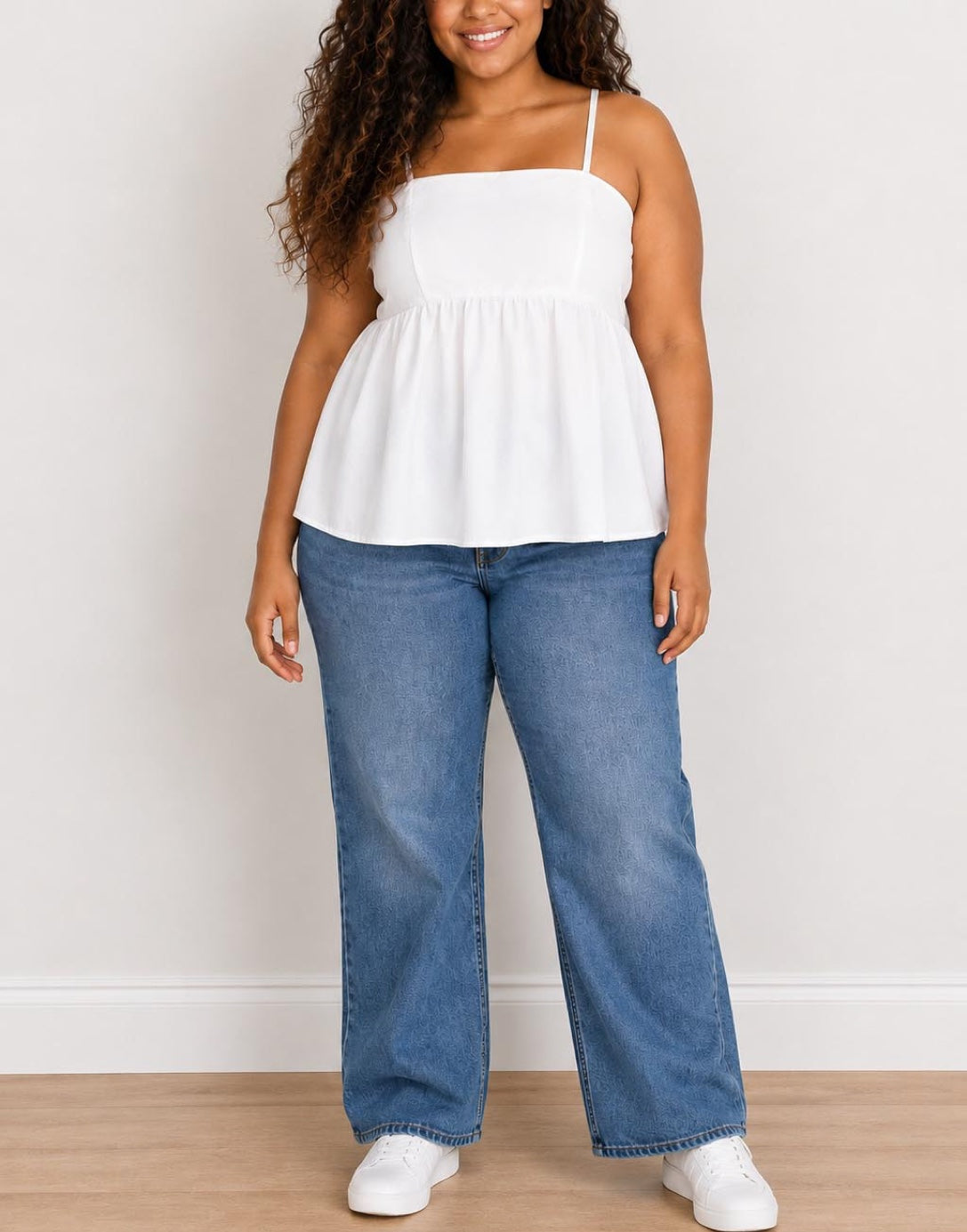 Woman wearing a white Plus Size Bow Back Babydoll Cami Top and blue jeans against a plain background