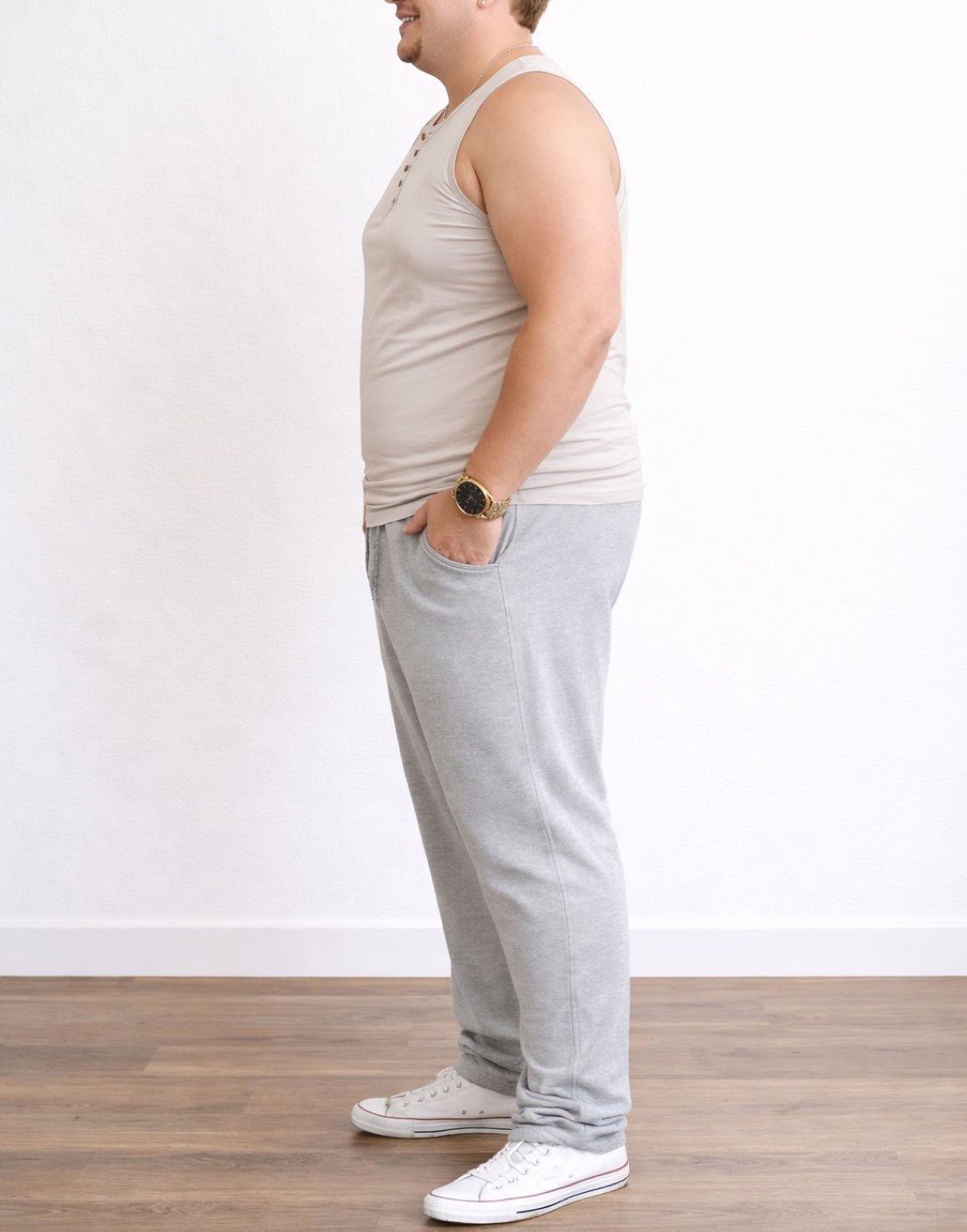 Side view of man wearing a beige Plus Size Button Front Round Neck Tank Top and gray sweatpants on a plain background.