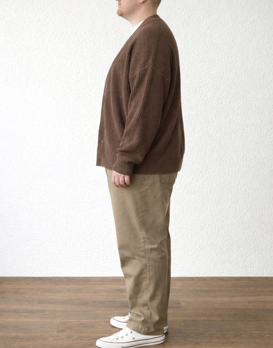 Side view of person wearing a brown Plus Size Button Front Cardigan and beige pants standing against a white wall.