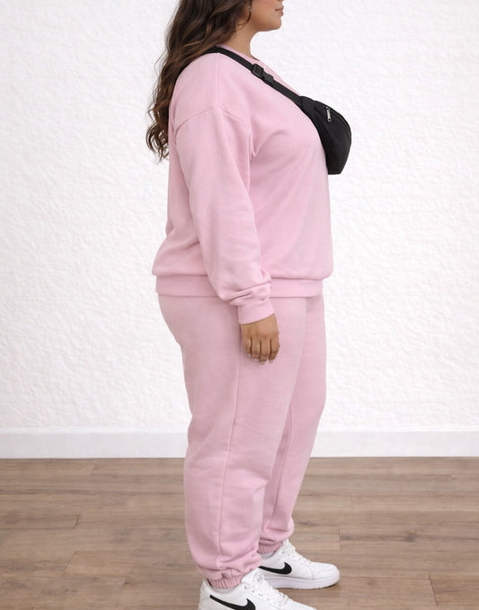 Person wearing a pink Plus Size tracksuit with a black bag over one shoulder on a white background