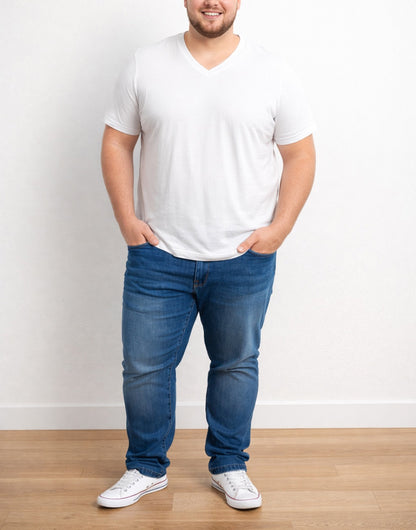 Man wearing a white Plus Size Classic V-Neck T-Shirt and blue jeans standing against a plain white wall.
