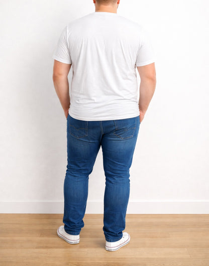 Back view of person wearing a white Plus Size Classic T-Shirt and blue jeans standing against a white wall.