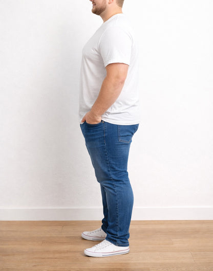 Side view of man wearing a white Plus Size Classic V-Neck Tee Shirt and blue jeans standing against a plain white wall.