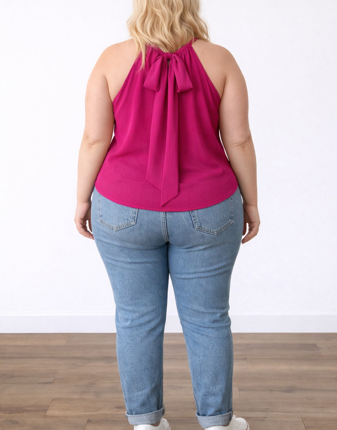 Back view of woman wearing a pink Plus Size Halter Top and blue jeans on a white background