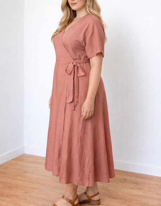 Side view of woman wearing a pink Plus Size Wrap Dress with a white background.
