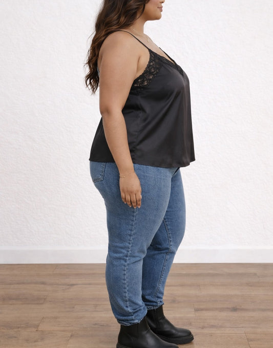 Side view of woman wearing a black Plus Size Lace-Trim Cami Top and blue jeans on a white background.