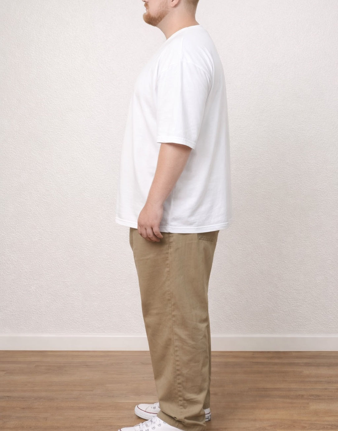Side view of person wearing a white Plus Size Men Oversized Longline Tee and beige pants against a plain background.