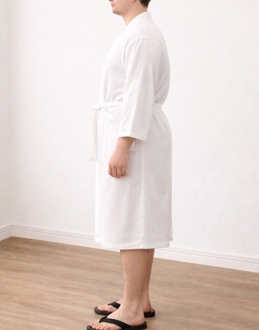 Side view of person wearing a white bathrobe standing on a wooden floor against a white wall.